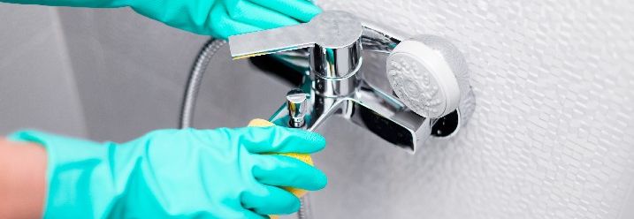 Person mit Handschuhen reinigt eine Duscharmatur.